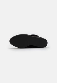 Semelle de chaussure noire avec surface en caoutchouc texturé, forme arrondie et design minimaliste. Aucun logo ou motif visible.