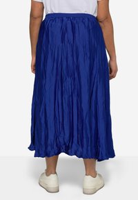 Falda maxi plisada azul hecha de una tela ligera, con cintura elástica y un diseño fluido, combinada con zapatillas blancas.