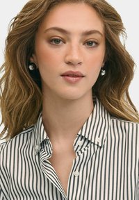Pruhovaná košile s knoflíkovým límcem, zdobená tenkými černobílými pruhy. Model doplnil kulatými náušnicemi, které ukazují hladkou texturu.