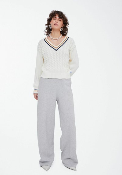 Cream sweater with cable knit pattern and navy stripe detail at the neckline, paired with light gray wide-leg sweatpants and pointed shoes.