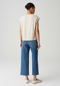 Cremfarbener Kurzarm-Top kombiniert mit dunkelblauen weiten Jeans. Die Schuhe sind hellbeige und haben eine weiche Textur. Einfaches und modernes Design.