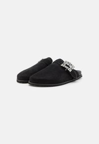 Črne nubuk slip-on čevlje z zaobljenim nosom in dekorativno sponko iz kristalov na pasu. Podplat je raven in strukturen za boljši oprijem.