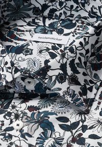 Camicia bianca con motivo floreale in blu scuro e marrone, con bottoni bianchi, dotata di etichetta "seidensticker" sul colletto.
