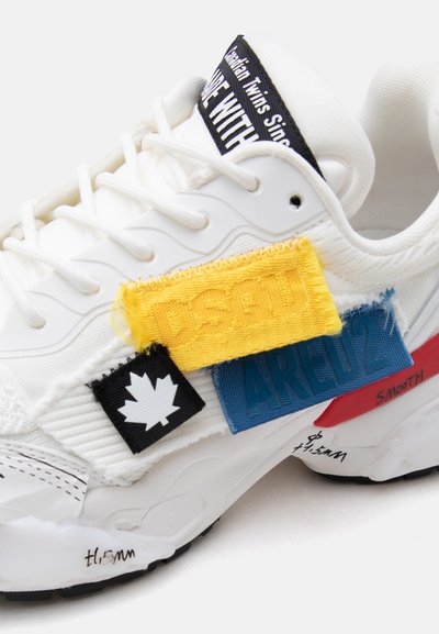 Λευκό αθλητικό παπούτσι με στρωματοποιημένα υφασμάτινα μπαλώματα σε κίτρινο, μπλε, μαύρο και κόκκινο, με λογότυπο φύλλου σφενδάμου και εκτυπωμένο κείμενο στη σόλα και τη γλώσσα.