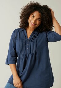 Blusa blu navy a maniche lunghe con patta di bottoni, dettagli plissettati e vestibilità comoda. Tessuto morbido con una superficie liscia.