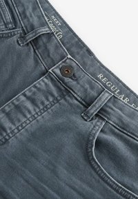 Jeans en denim gris avec une texture lisse, dotés d'une fermeture à bouton, de passants de ceinture et d'un design classique à cinq poches, étiquetés "COUPE CLASSIQUE".