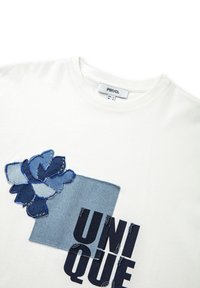 Witte katoenen t-shirt met een denim patch en geborduurd bloemenontwerp in het blauw. Het woord "UNIQUE" is gedrukt in vette, donkere letters.