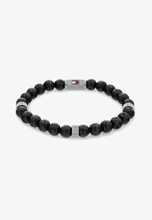 Crna narukvica od lave s srebrnim akcentima i pravokutnim amblemom s crvenim, bijelim i plavim prugama. Okruge perle stvaraju teksturirani izgled.