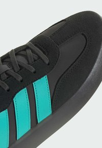 Czarny sneaker z paskami z tkaniny w kolorze teal. Posiada chropowatą cholewkę z zamszu i gładką gumową podeszwę. Sznurowadła w dopasowanym czarnym kolorze.