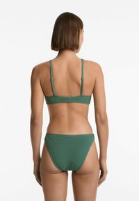 Grön texturerad bikinitopp och trosa med vävd design, justerbara remmar och klassisk skärning. Bakifrån framhäver simklädets enkelhet.