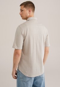 C�ămașă cu mânecă scurtă, cu model geometric, de culoare bej deschis, având guler cu colier întors și tiv curbat. Textura stofei este casual.