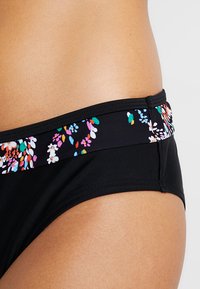 Svart bikiniunderdel med ett blommönstrat midjeband med färgglada accenter, tillverkad av elastiskt tyg för komfort och passform.