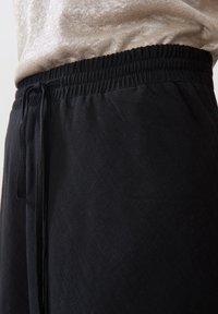 Mustat joogahousut, joissa on joustava vyötärö ja naru, jossa on kohokuvioitu kangas ja kapeneva lahjesuunnittelu muodikkaan ilmeen saavuttamiseksi.