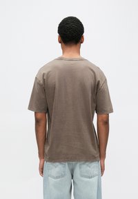 Καφέ κοντομάνικο μπλουζάκι με στρογγυλή λαιμόκοψη και άνετη γραμμή. Διαθέτει μαλακό, υφασμάτινο βαμβάκι με υφή και απλό σχέδιο.