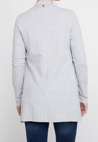 Harmaa pitkähihainen paita, jossa on hieman levenevä helma, kaulus ja saumat, sekä pieni logo niskan takana.