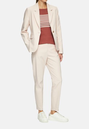 Blazer rosa claro sobre un suéter a rayas color óxido, combinado con pantalones rosa claro y zapatillas blancas. Tejido suave con un corte ajustado.