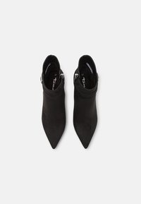 Bottines noires en suède, avec un bout pointu, un design à revers, et des accents en métal argenté. Étiquette de taille visible à l'intérieur.