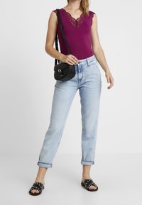 Bodysuit fucsia con escote de encaje, jeans de tiro alto azul claro, bolso bandolera negro y sandalias negras de deslizar con acentos de tachuelas.