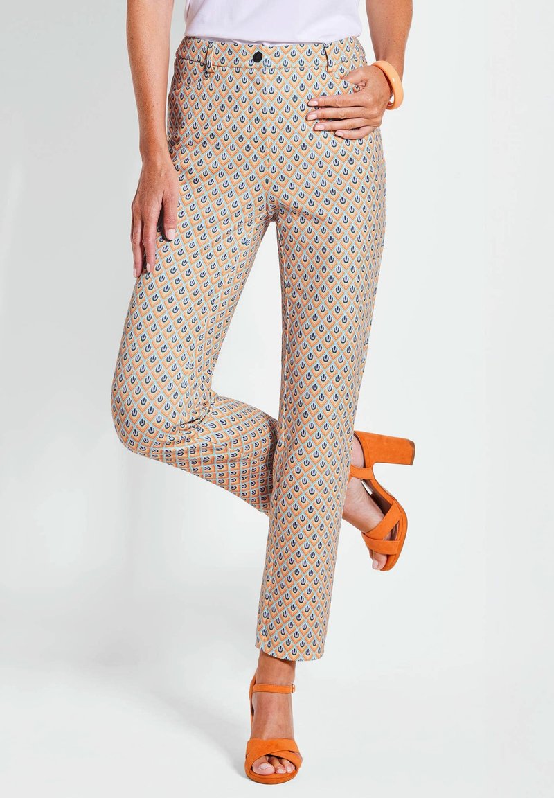 Pantaloni a fantasia in arancione chiaro, con un motivo geometrico blu e arancione scuro; abbinati a sandali open-toe arancioni.