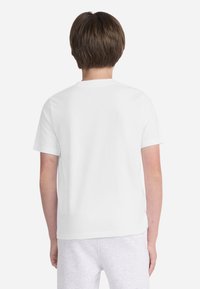 T-shirt blanc à manches courtes avec un col rond, présentant une texture douce en coton et sans motifs ni graphismes visibles.