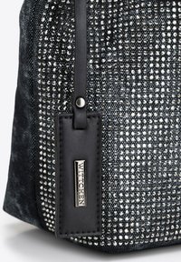Zwarte handtas met textuur, voorzien van een stoffen oppervlak versierd met zilveren pailletten en een zwart leren label met een metalen gravure.