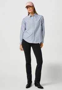 Camisa de botones a rayas azul y blanca con un bolsillo, combinada con jeans negros ajustados y una gorra rosa claro. Tejido suave y corte entallado.