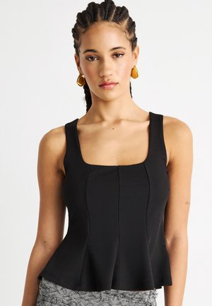 Kvinne med flette og gyldne hoops-øreringer, iført en tettsittende svart ermeløs topp med firkantet utringning.