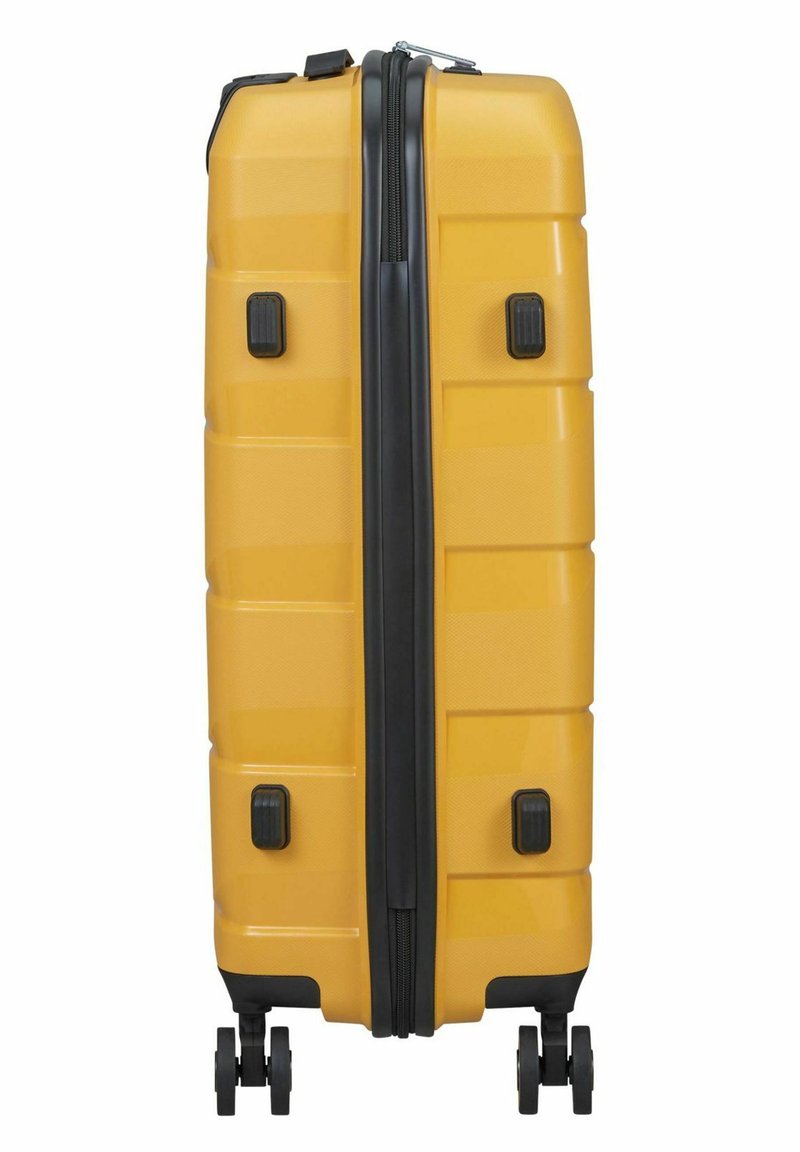 Gele harde koffer rechtopstaand met vier zwarte wielen en een centrale zwarte rits.