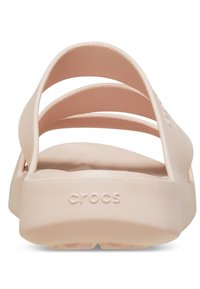 Różowe klapki Crocs z gładką teksturą, otwartym tyłem i trzema szerokimi paskami. Posiadają wytłoczone logo oraz wyprofilowaną wkładkę dla komfortu.