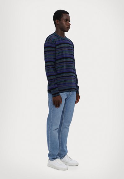 Maglione a maniche lunghe blu navy con strisce orizzontali multicolori, abbinato a jeans azzurri chiari e sneaker bianche. Dimostra uno stile e una vestibilità casual.