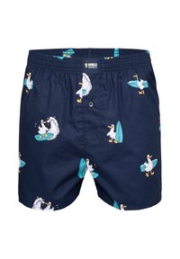 Boxers bleu marine avec un motif répétitif de canards blancs tenant des planches de surf turquoise et surfant sur les vagues. Ceinture élastique avec braguette à boutons.