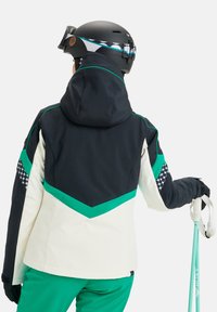 Veste de ski avec un schéma de couleurs noir, vert et crème ; elle possède une capuche, des motifs géométriques, et est accompagnée de bâtons de ski turquoise.