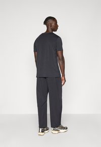 Black short-sleeve t-shirt paired with loose black pants, showcasing a smooth texture and simple design. Footwear features black and gold accents.