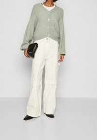 Světlounce zelený, zkrácený kardigan se zapínáním na knoflíky, kombinovaný s bílými volnými kalhotami a černými botami s špičatou špičkou. Součástí je také černá kabelka na poutech.