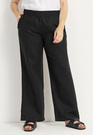 Schwarze, weit geschnittene Hose aus leichtem Leinen mit elastischem Bund und Seitentaschen, kombiniert mit schwarzen Sandalen.