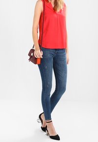 Röd ärmlös blus med V-ringning, matchad med blå skinny jeans. Svarta klackar med vit detalj, och en liten bordeaux korsväska.