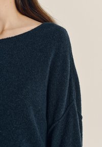 Mørkeblå striktrøje med off-shoulder design, blød tekstur, løs pasform og droppe skuldre, der viser minimalistisk detaljer.