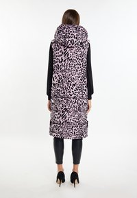 Padded Weste in Pink mit einem schwarzen Leopardenmuster, ausgestattet mit einer großen Kapuze, seitlichen Taschen und einer gesteppte Textur. Kombiniert mit schwarzen Leggings und hohen Schuhen.