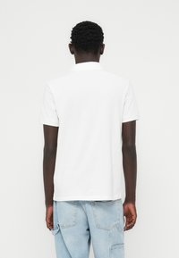 Άσπρο κοντομάνικο πόλο με γιακά, με ομαλή υφή και ίσια κοπή, σε συνδυασμό με ανοιχτόχρωμο τζιν και τσέπες.