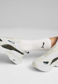 Ljusfärgade sneakers med texturerat mesh och syntetiska detaljer, som har en kraftig sula. En vit strumpa visar en svart logotyp på kanten.