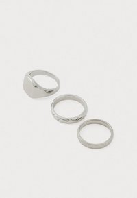 Três anéis de prata: um anel de sinete liso, um anel torcido com um detalhe e um anel plano simples, todos com um acabamento metálico polido.