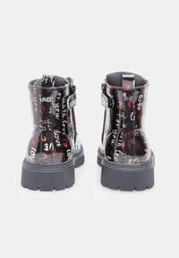 Botine negre din piele la patent, cu talpă texturată masivă, cuvinte decorative scrise de mână în culori multiple și închidere cu fermoar pe lateral.