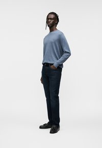 Chemise bleue à manches longues en tissu doux, associée à un jean denim foncé, portée avec des chaussures noires. Design simple, coupe décontractée, sans motifs distincts.