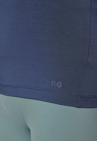 Mørkeblå tett sportsbluse med glatt tekstur og subtil logo i kanten, parret med lysegrønne tights med stretch.