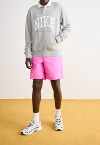 Szara bluza z białym logo "NIKE", różowe spodenki i białe skarpetki do kostek. Obuwie stanowią szaro-czarne buty sportowe z detalami.