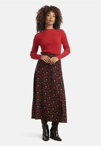 Red ribbed long-sleeve top paired with a black skirt featuring a red and pink polka dot pattern, styled with knee-high black boots.