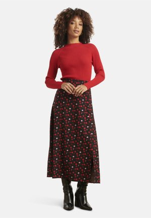 Rood geribbelde lange mouw top gecombineerd met een zwarte rok met een rood en roze stippenpatroon, gestyled met kniehoge zwarte laarzen.