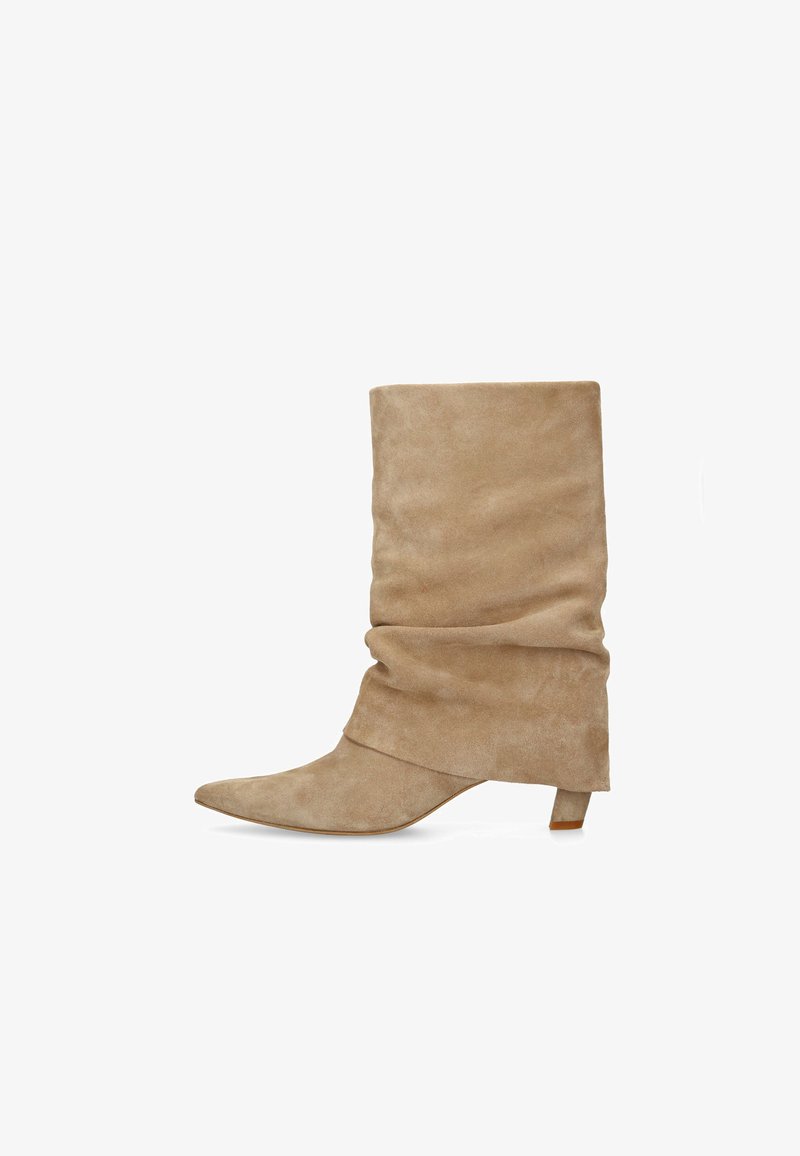Beige suède laarzen tot halverwege de kuit met een slouchy uitstraling, een puntige neus en lage kittenhak, afgebeeld tegen een witte achtergrond.