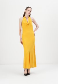 Robe maxi jaune à col halter avec un décolleté drapé, un corsage ajusté et un ourlet évasé ; texture lisse et design minimaliste. Talons hauts noirs.