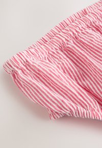 Lähikuva kuva vaaleanpunavalkoraidallisesta joustavasta vyötärönauhasta ja kevyen vaatteen poimutetusta kankaasta.